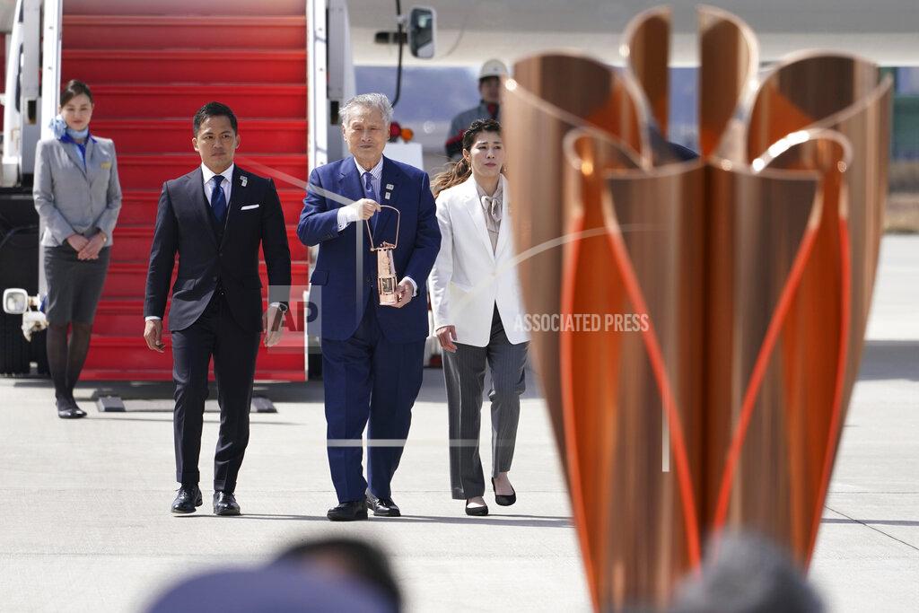 Tokyo 2020 Olympics chief Yoshiro Mori, center, followed by three-time Olympic gold medalists Tadahiro Nomura and Saori Yoshida, right, carries the Olympic flame during the Flame Arrival Ceremony at Japan Air Self-Defense Force Matsushima Base in Higashimatsushima in Miyagi Prefecture, north of Tokyo, Friday, March 20, 2020. The Olympic flame from Greece arrived in Japan even as the opening of the the Tokyo Games in four months is in doubt with more voices suggesting the games should to be postponed or canceled because of the worldwide virus pandemic. (AP Photo/Eugene Hoshiko)