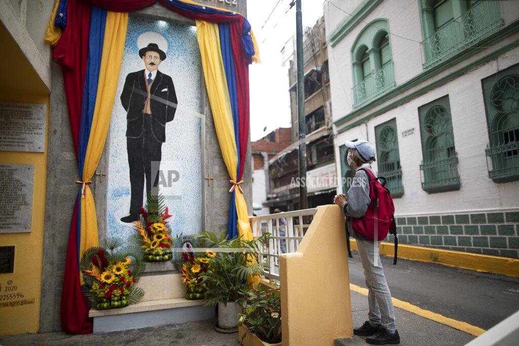 Ariana Cubillos A woman prays close to a painting of Venezuelan popular saint, Dr. Jose Gregorio Hernandez at the street where he died in a car accident in 1919, in La Pastora neighborhood of Caracas, Venezuela, Wednesday, April 28, 2021. Known as the "doctor of the poor, Hernandez is set to be beatified by the Catholic church, a step towards sainthood, on April 30th. (AP Photo/Ariana Cubillos)