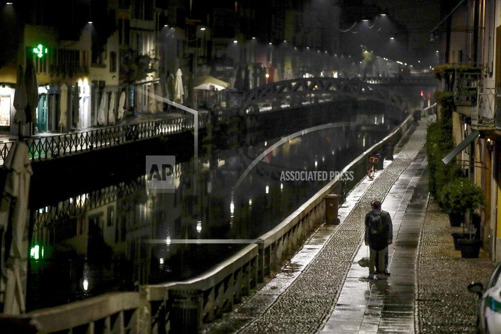 Luca Bruno A man stands on the unusually empty Navigli area, a popular evening spot of restaurants and pubs along canals in Milan, Italy, Thursday, Oct. 22, 2020, as authorities imposed curfews in a bid to slow the spread of COVID-19. (AP Photo/Luca Bruno)