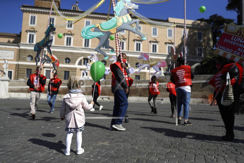 Gregorio Borgia A child holds a balloon as she looks at amusement park workers holding a makeshift carousel as they join with circus workers in a demonstration demanding more support from the Italian government as their activities are shut down since the start of the COVID-19 outbreak, in Rome's Piazza del Popolo, Friday, March 26, 2021,. (AP Photo/Gregorio Borgia)