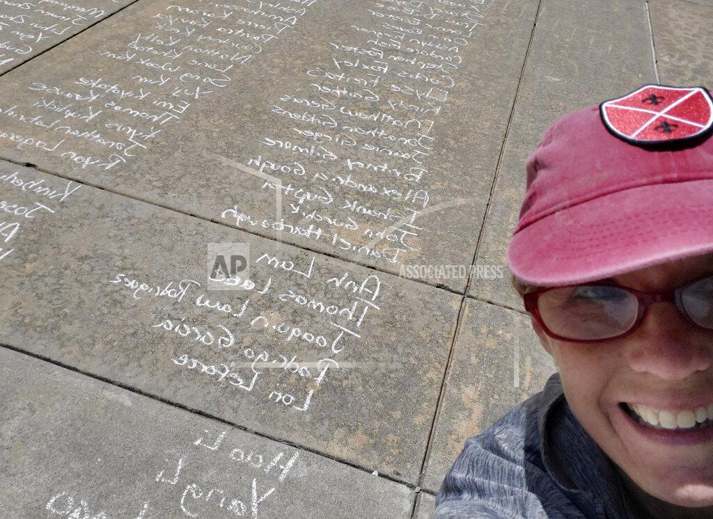 In this May 8, 2020 photo, Kim Gaddie, an Associate Senior Fellow at Headington College, takes a selfie photo of herself with a long list of University of Oklahoma graduate names written on the sidewalk outside of the Gaylord Family-Oklahoma Memorial Stadium in Norman, Okla.. Gaddie and several staff members spent hours writing more than 4,000 names of the 2020 graduates who were unable to have their in-person commencement ceremony due to COVID-19. (Courtesy of Kim Gaddie via AP)