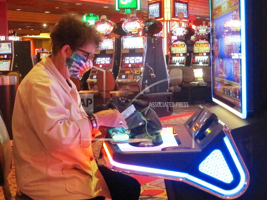 Wayne Parry This June 23, 2021 photo shows a woman taking money out of her purse at a slot machine at Bally's casino in Atlantic City, N.J. Figures released on Sept. 16, 2021 show the Atlantic City casinos and the three racetracks that offer sports betting collectively won over $427 million in August, 31% more than they did in August 2020 as the casinos were just emerging from coronavirus-related closures. (AP Photo/Wayne Parry)