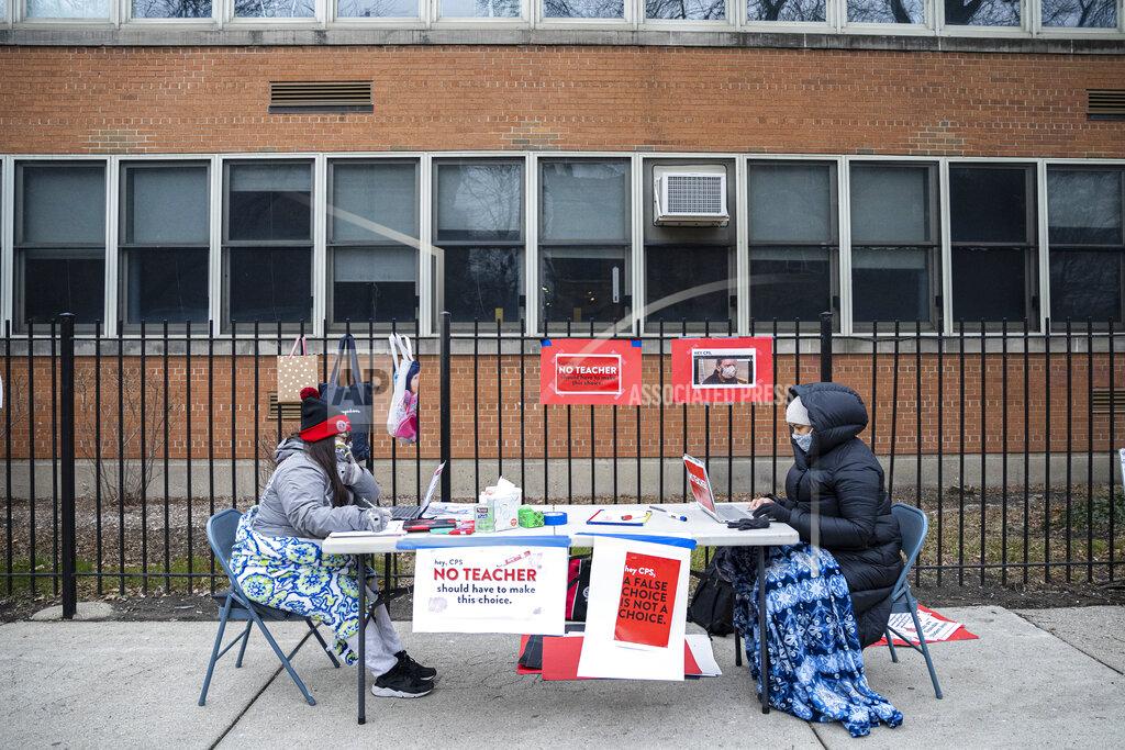Anthony Vazquez FILE - In this Monday, Jan. 11, 2021 file photo, teachers Adrienne Thomas, left, and Irene Barrera, right set up their computers and materials for their virtual classes outside of Suder Montessori Magnet Elementary School in solidarity with pre-K educators forced back into the building in Chicago. The Chicago Teachers Union said Sunday, Jan. 24 that its members voted to defy an order to return to the classroom before they are vaccinated against the coronavirus, setting up a showdown with district officials who have said such a move would amount to an illegal strike.(Anthony Vazquez/Chicago Sun-Times via AP)
