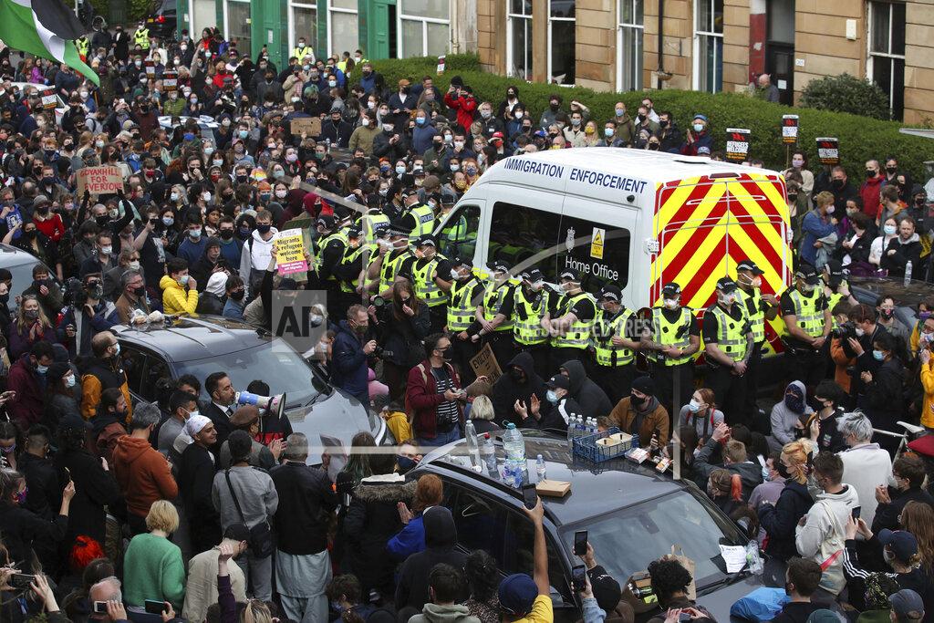 Andrew Milligan Lawyer Aamer Anwar, at left with megaphone, speaks to protesters blocking the road as police surround an immigration van in Kenmure Street, Thursday May 13, 2021, in Glasgow, Scotland. Protesters blockaded a street in Glasgow on Thursday in a seven-hour standoff which successfully forced the release of two men detained by U.K. immigration authorities. Hundreds of demonstrators filled the road in Scotland’s largest city to prevent a van leaving with the men inside, before police finally announced they would be freed. (Andrew Milligan/PA via AP)