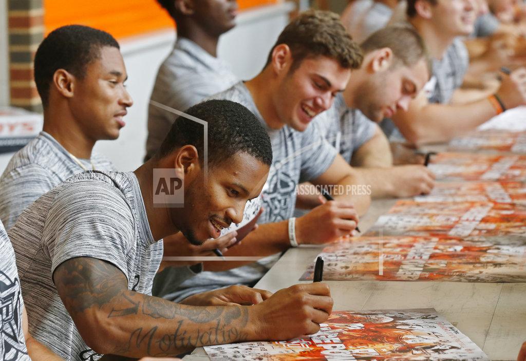 Oklahoma State wide receiver Tyron Johnson, front, signs an autograph as he sits with teammates Jalen McCleskey, left, and Dillon Stoner, right, during the NCAA college football team's fan appreciation day in Stillwater, Okla., Saturday, Aug. 4, 2018. (AP Photo/Sue Ogrocki)