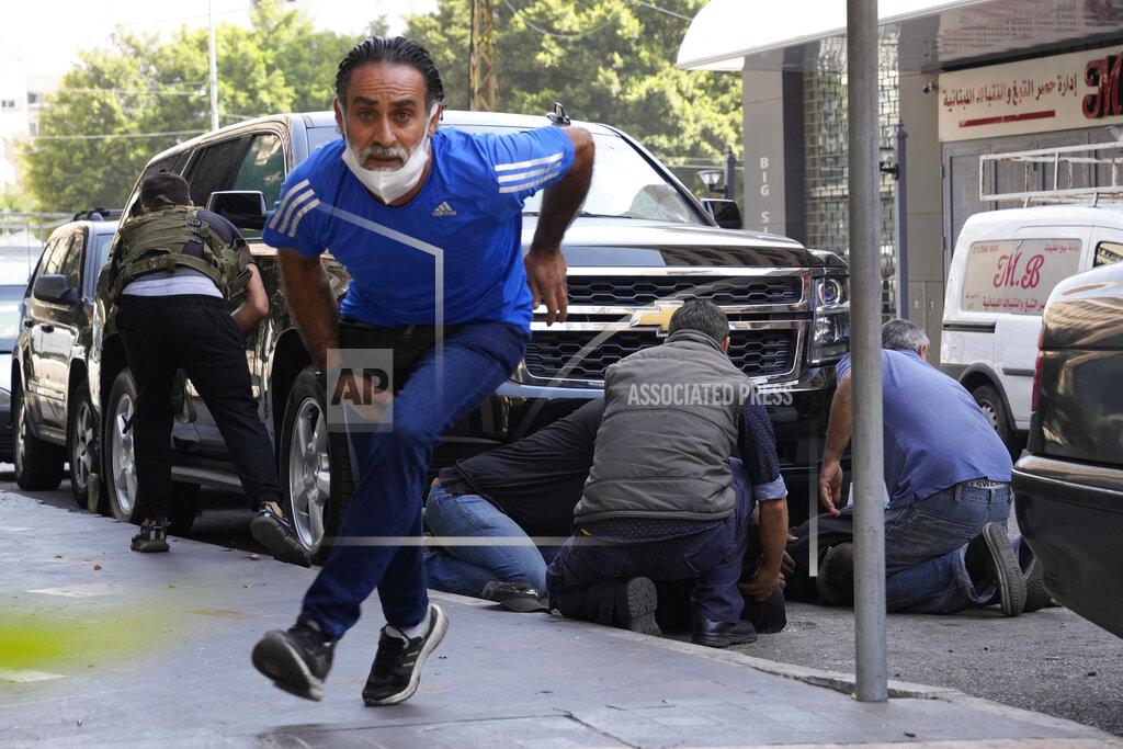 Hassan Ammar FILE - In this Oct. 14, 2021, file photo, a man runs to take cover as supporters of a Shiite group allied with Hezbollah help injured men during armed clashes that erupted during a protest in the southern Beirut suburb of Dahiyeh, Lebanon. The shootout on the streets of Beirut between rival Christian and Muslim groups has revived memories of the country's 1975-90 civil war and fired up sectarian passions in a country that never dealt with the causes of its violent past. (AP Photo/Hassan Ammar, File)