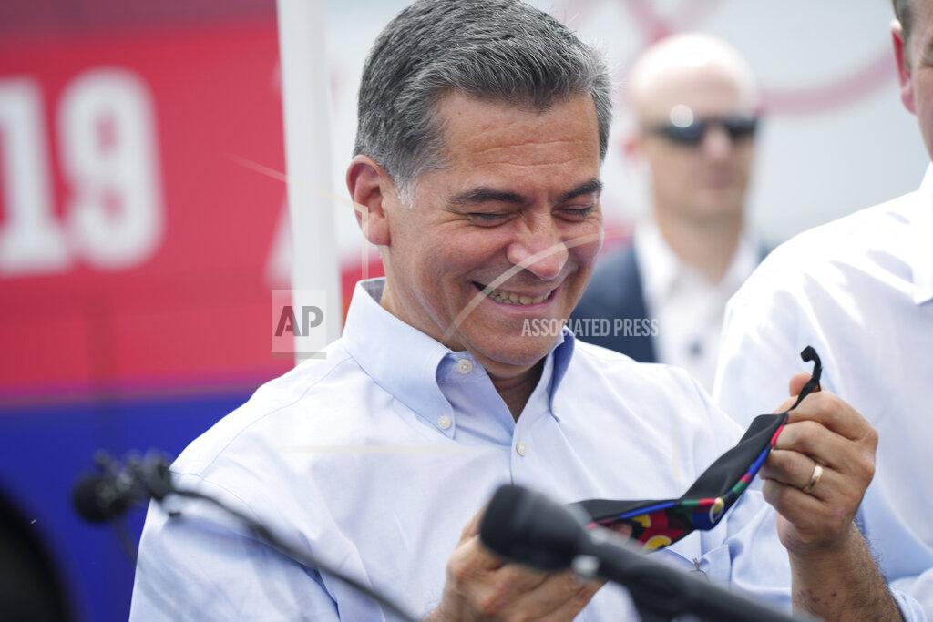 David Zalubowski U.S. Department of Health and Human Services Secretary Xavier Becerra at a Colorado-themed mask given to him by U.S. Rep. Jason Crow, D-Colo., during a visit to a pair of buses set up as traveling clinics as part of the state's "Vaccines For All" campaign Friday, June 18, 2021, in Aurora, Colo. The buses are being used to distribute COVID-19 vaccines. (AP Photo/David Zalubowski)