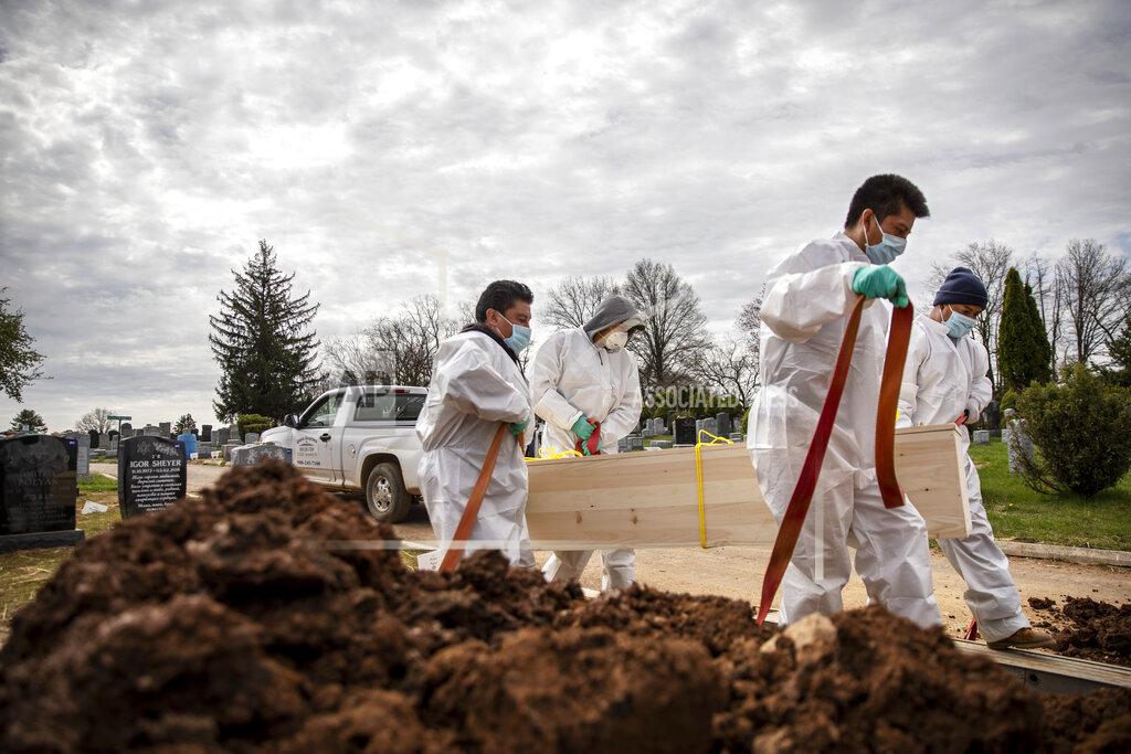 David Goldman Gravediggers carry the casket of someone presumed to have died from coronavirus as they are buried without any family present at Mount Richmond Cemetery in the Staten Island borough of New York, Tuesday, April 7, 2020. In a marathon of grief at this small Jewish cemetery mounds of dirt are piling up as graves are opened, vans are constantly arriving with bodies aboard and a line of white signs is being pressed into the ground marking plots soon to be occupied. Families are being kept away from their loved one's gravesite at the cemetery, which caters to those with little or nothing. (AP Photo/David Goldman)