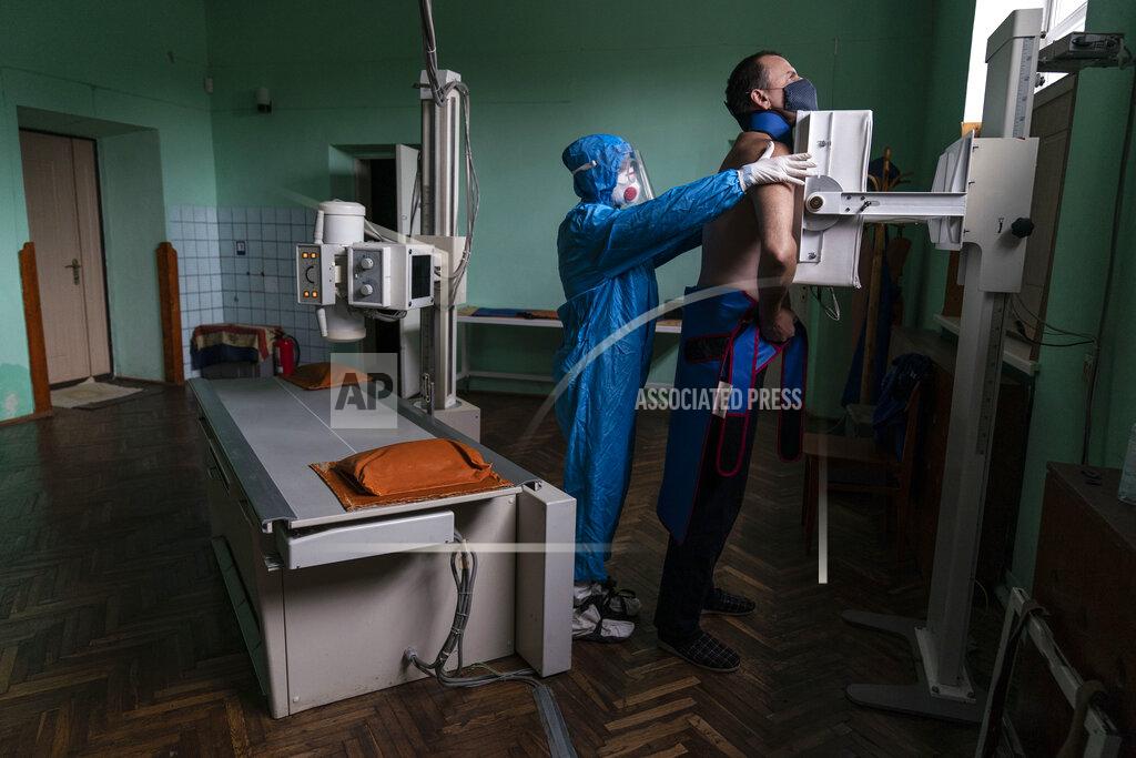Evgeniy Maloletka A medic prepares a coronavirus patient for a lung X-ray at a hospital in Stryi, Ukraine, Tuesday, Sept. 29, 2020. Coronavirus infections in Ukraine began surging in late summer, and the ripples are hitting towns in the western part of the country. The government wants to avoid imposing a new lockdown, but officials acknowledge that the rising infections could make it necessary. (AP Photo/Evgeniy Maloletka)