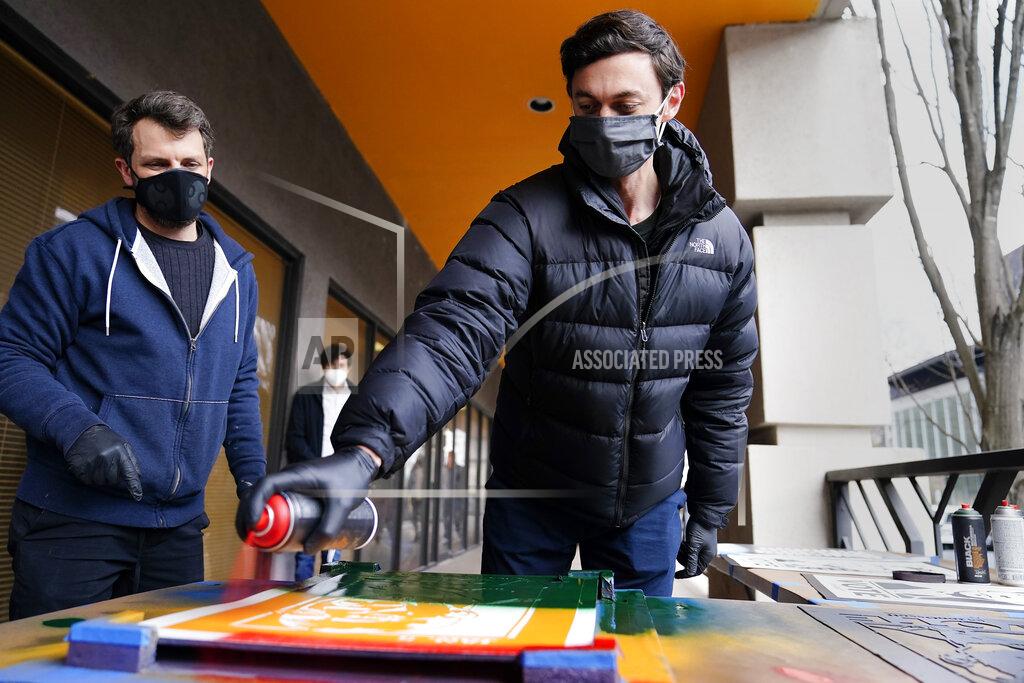 Brynn Anderson U.S. Senator-elect Jon Ossoff, D-Ga., right, spray paints a campaign poster with Brandon Litman, 39, left, of Brooklyn, N.Y. after Georgia's Senate runoff race on Saturday, Jan. 9, 2021, in Atlanta. (AP Photo/Brynn Anderson)