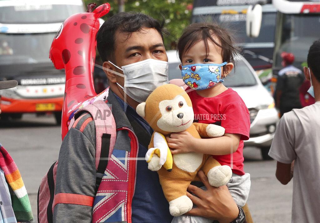 Tatan Syuflana A man carries his daughter at the Kalideres bus terminal in Jakarta, Indonesia, Wednesday, May 5, 2021. The mass exodus out of major cities in the world's most populous Muslim country is underway despite travel restrictions imposed by the government to prevent the spread of coronavirus outbreak, as people are heading home to their villages to celebrate Eid al-Fitr holiday that marks the end of the holy fasting month of Ramadan on May 13. (AP Photo/Tatan Syuflana)