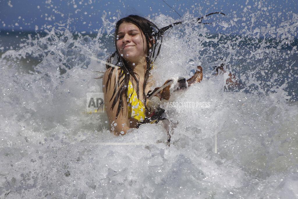 Matias Delacroix Mariana Rojas plays with her dog Sussy in the waves off Los Angeles beach after it recently reopened following a lockdown to contain the spread of COVID-19 in La Guaira, Venezuela, Friday, Oct. 23, 2020. Strict quarantine restrictions forced the closure of beaches across the country in March and reopened this week. (AP Photo/Matias Delacroix)