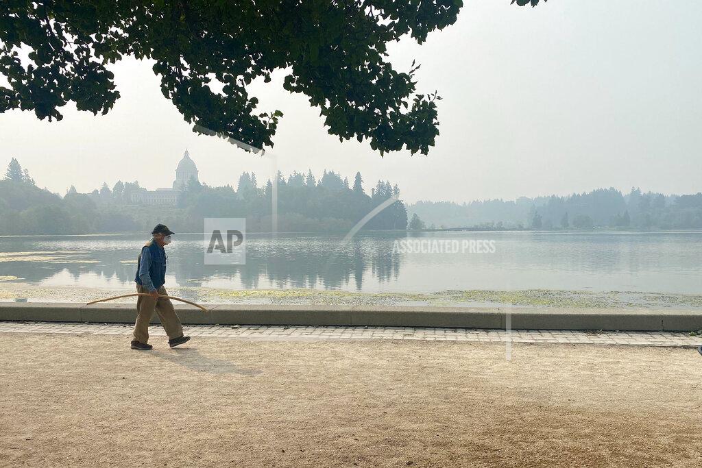 A man wearing a mask walks by the lake outside of the Washington State Capitol in Olympia, Wash., Friday, Sept. 11, 2020. Olympia is among the places facing unhealthy air quality due to wildfires in the Pacific Northwest. (AP Photo/Rachel La Corte)