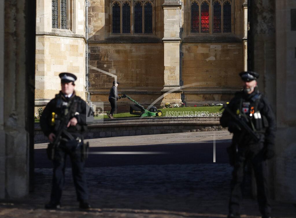Alastair Grant Armed police guard the King Henry VII gate as a groundsman mows the grass outside St George's Chapel at Windsor Castle in Windsor, England, Friday, April 16, 2021. Prince Philip husband of Britain's Queen Elizabeth II died April 9, aged 99, his funeral will take place Saturday at Windsor Castle in St George's Chapel. (AP Photo/Alastair Grant)