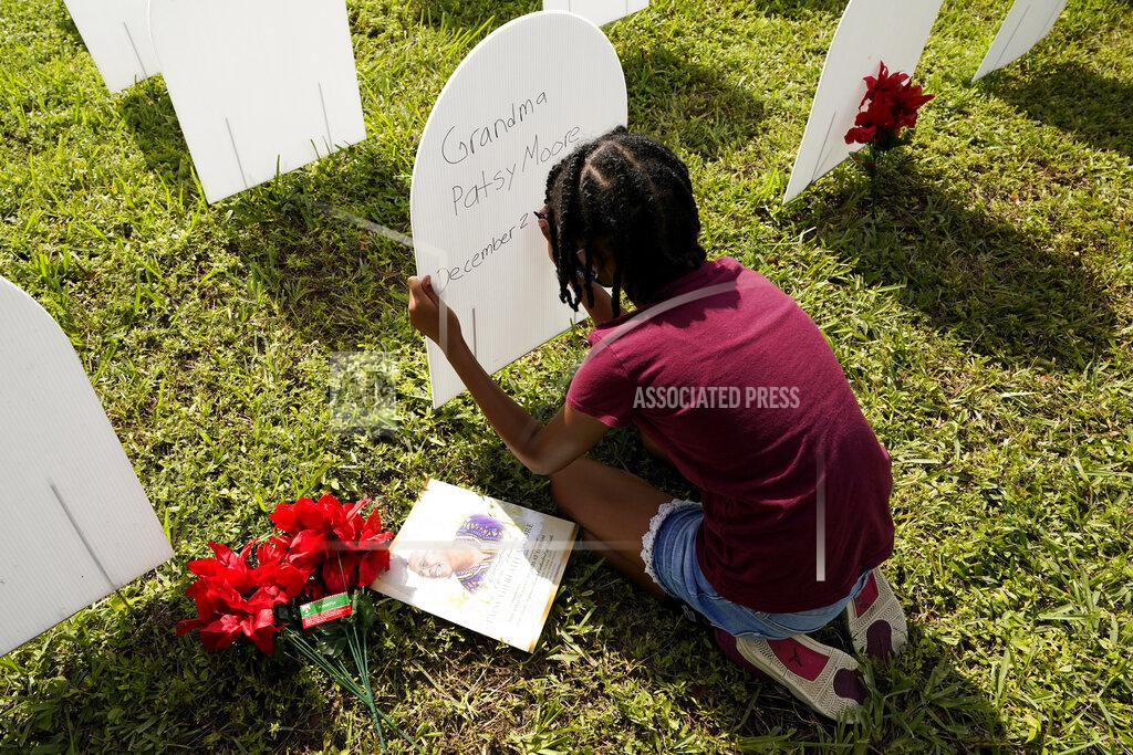 Lynne Sladky FILE - In this Nov. 24, 2020, file photo, Kyla Harris, 10, writes a tribute to her grandmother Patsy Gilreath Moore, who died at age 79 of COVID-19, at a symbolic cemetery created to remember and honor lives lost to COVID-19, in the Liberty City neighborhood of Miami. In Florida, more than 20,000 residents have died from COVID-19, tens of thousands have been hospitalized and more than a million caught it. (AP Photo/Lynne Sladky, File)