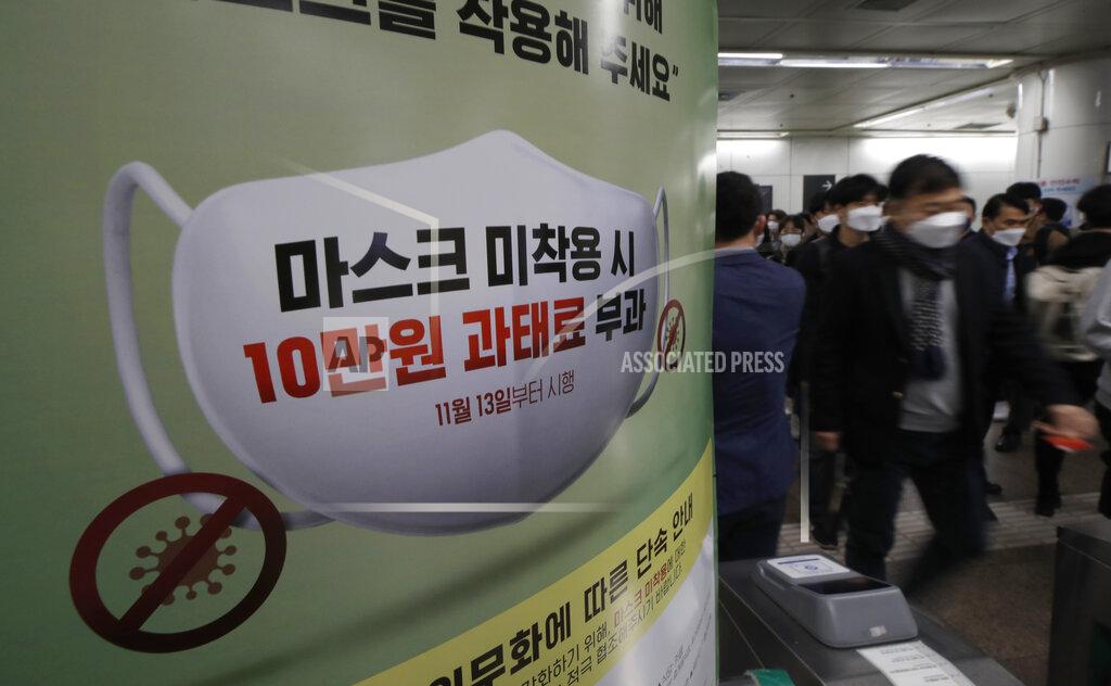 Lee Jin-Man People wearing face masks as a precaution against the coronavirus, walk past near a banner reading: "People who do not wear masks in public will face a 100,000 won ($90) fine", at a subway station in Seoul, South Korea, Friday, Nov. 13, 2020. South Korea has reported its biggest daily jump in COVID-19 cases in 70 days as the government began fining people who fail to wear masks in public. From Friday, officials started to impose fines of up to 100,000 won ($90) for people who fail to properly wear masks in public transport and a wide range of venues, including hospitals, nursing homes, pharmacies, nightclubs, karaoke bars, religious and sports facilities and at gatherings of more than 500 people. (AP Photo/Lee Jin-man)