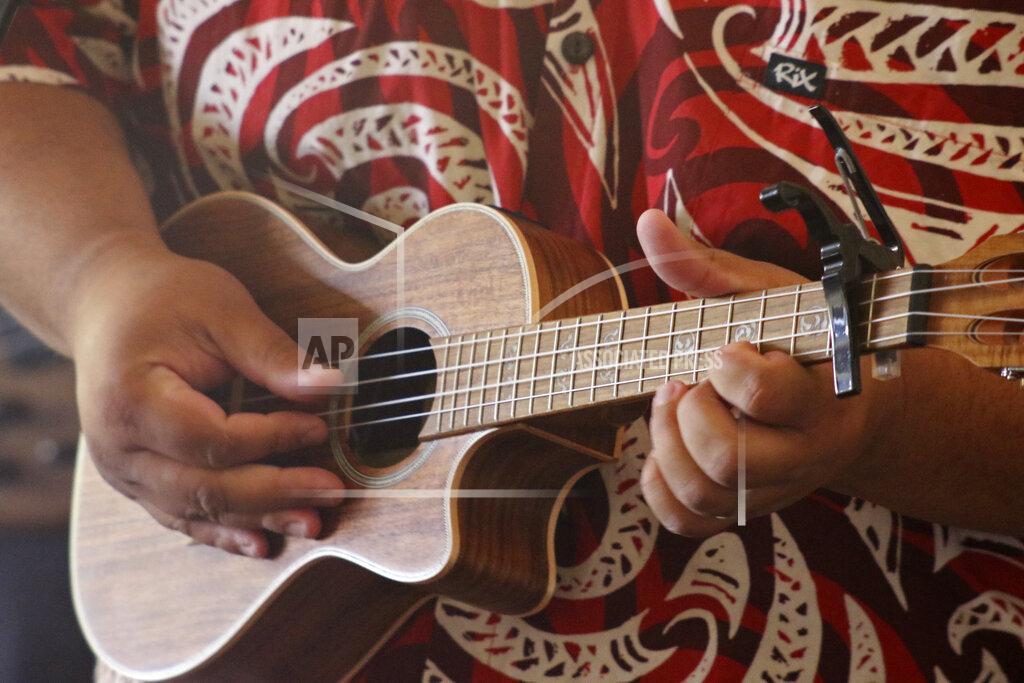 This May 5, 2020, photo shows Lance Chang playing a ukulele during a livestream performance of his family's band, Kanilau, from the living room of his father Roland Chang's home in Honolulu. The coronavirus pandemic has taken out large sections of Hawaii's tourism-based economy, including the Chang family's turtle and dolphin snorkel tour business and their regular music gig in Waikiki. (AP Photo/Audrey McAvoy)