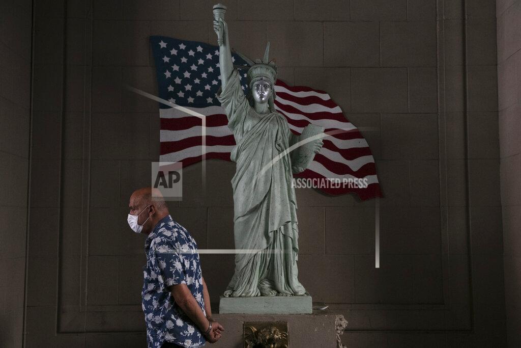 Jae C. Hong FILE - In this June 22, 2020, file photo, a man with a face mask walks past a replica of Statue of Liberty in Los Angeles. (AP Photo/Jae C. Hong, File)