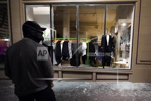 FILE - In this Nov. 4, 2020, file photo, a man stands in front of a broken display window at a retail store during protests in Portland, Ore. Police in Portland say they believe a new state law prohibits officers from directly intervening when people smash storefronts and cause mayhem. The measure passed this year prohibits the use of crowd control methods like pepper spray and rubber bullets "unless use of force is otherwise authorized by statute." (AP Photo/Marcio Jose Sanchez, File)