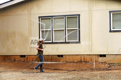 Katie Wright hoses down a family home on Casa Drive in an evacuated neighborhood about a half-mile from the Fawn Fire near Redding, Calif., on Thursday, Sept. 23, 2021. Evacuations have been ordered in a Northern California community as a new wildfire spreads. (Mike Chapman/The Record Searchlight via AP)