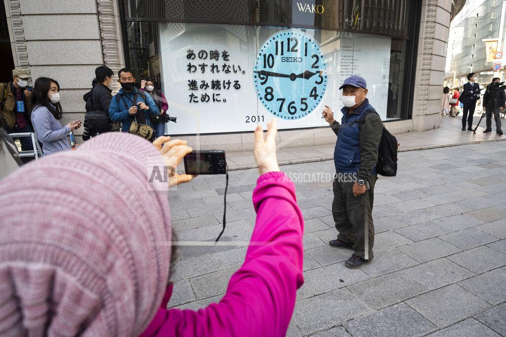 Hiro Komae A woman takes a photo of her husband in front of a clock that shows 2:46 p.m. to commemorate the 2011 earthquake that hit the northeastern Japan, before the 10th anniversary to pay tribute to the victims in Tokyo Thursday, March 11, 2021. Japan is marking the 10th anniversary Thursday of the earthquake, tsunami and nuclear disaster that hit the northeastern region. (AP Photo/Hiro Komae)