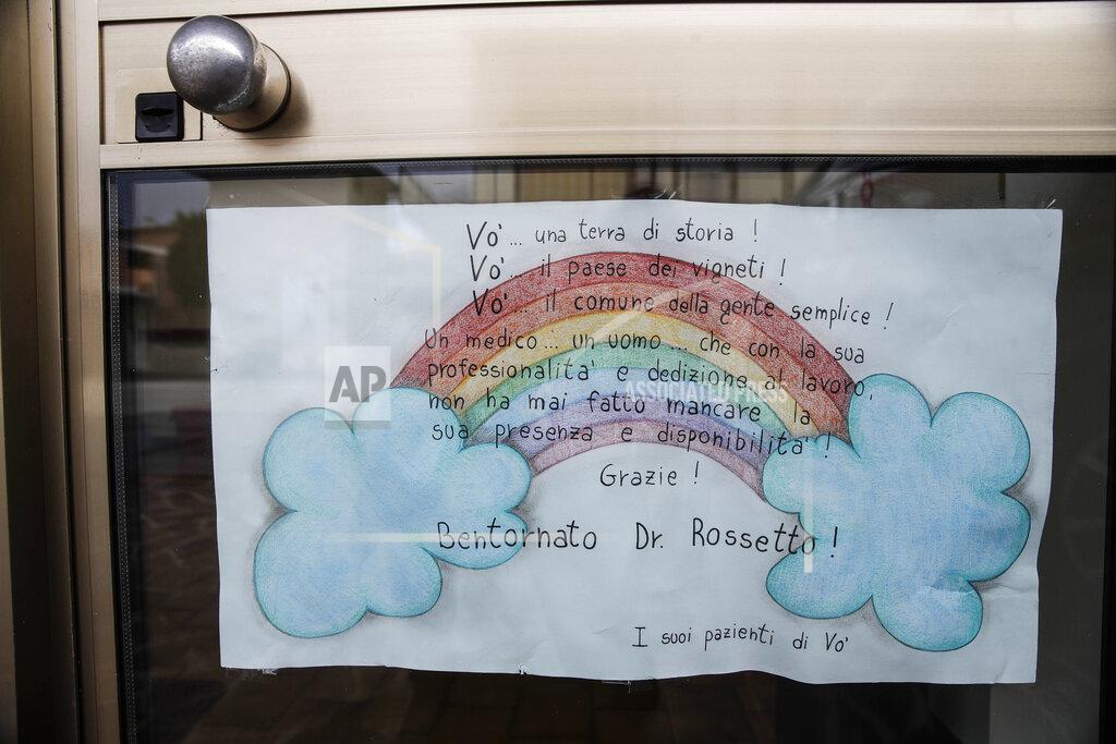 Luca Bruno A poster made by patients hangs on the door of doctor Luca Rossetto's medical office in Vo Euganeo, northern Italy, Wednesday, Feb. 10, 2021. Shockwaves ran through the wine-making village of Vo, west of Venice, as word spread last Feb. 21 that a retired roofer had died of the new coronavirus becoming the first known COVID-19 victim in the West. Writing on poster reads in Italian; "Vo... a land of history! Vo'...a town of vineyards! Vo'...the council of simple people! A doctor...a man...who with his professionalism and dedication to work never missed his presence and availability! Thank you! Welcome Dr. Rossetto!" (AP Photo/Luca Bruno)
