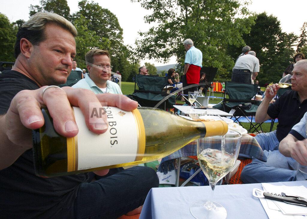 FILE - In this July 7, 2006 file photo, Michael Van Parks, left, pours wine with friends, Bill Beeman, center, and Don Usher, right, all of West Hartford, Conn., while having a picnic on the lawn at Tanglewood in Lenox, Mass. before the start of Boston Symphony Orchestra's opening night. The Boston Symphony Orchestra announced Friday, March 19, 2021 that its 2021 outdoor season at Tanglewood, the acclaimed symphony's summer home in the Berkshires of western Massachusetts, will feature a return to live, in-person concerts from July 9 to Aug. 16. The event was canceled in 2020 due to the COVID-19 pandemic. (AP Photo/Michael Dwyer, File)