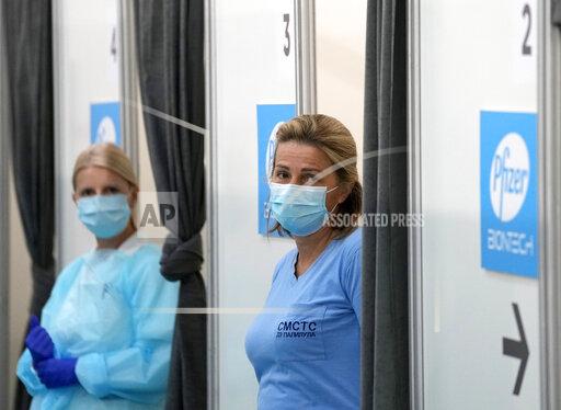 FILE - In this Saturday, Oct. 2, 2021 file photo, medical workers wearing protective gear wait to administer the COVID-19 vaccine, at Belgrade Fair makeshift vaccination center, Serbia. Serbia on Wednesday Oct. 20, 2021, introduced COVID-19 passes for indoor venues late at night following weeks of surging infections and relatively low vaccination rates. (AP Photo/Darko Vojinovic, File)