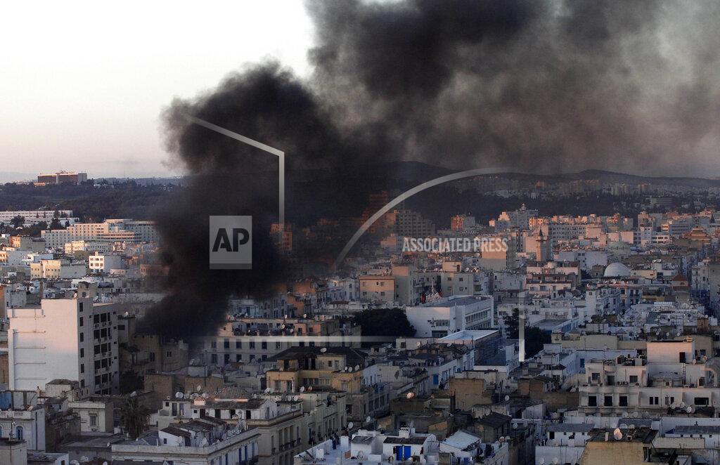 Christophe Ena FILE - In this file photo dated Friday, Jan. 14, 2011, a column of smoke rises from buildings during clashes between protesters and police in Tunis. Tunisia's president declared a state of emergency and announced that he would fire his government as violent protests escalated Friday, with gunfire echoing in the North African country's usually calm capital and police lobbing tear gas at protesters. On Thursday Jan. 14, 2021, Tunisia commemorates 10 years since the flight into exile of its iron-fisted leader, Zine El Abidine Ben Ali, pushed from power in a popular revolt that foreshadowed the so-called Arab Spring.(AP Photo/Christophe Ena)