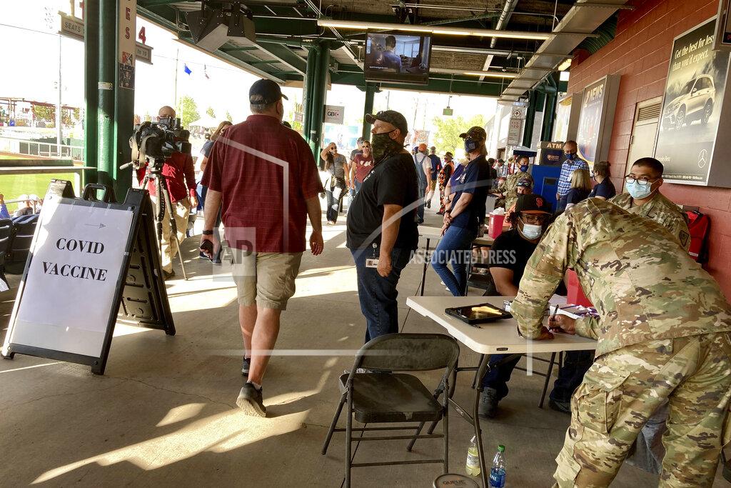 Scott Sonner People pass by a temporary vaccination clinic the Washoe County Health District organized with help from the Nevada National Guard offering free COVID-19 shots at the home season opener for the Reno Aces Triple-A minor league baseball team against the Las Vegas Aviators in Reno, Nev., on May 13, 2021. It's one of a series of pop-up clinics health officials are hosting around the state to help combat a drop-off in demand for vaccinations. Free shots will continue at all home games this summer. (AP Photo/Scott Sonner)