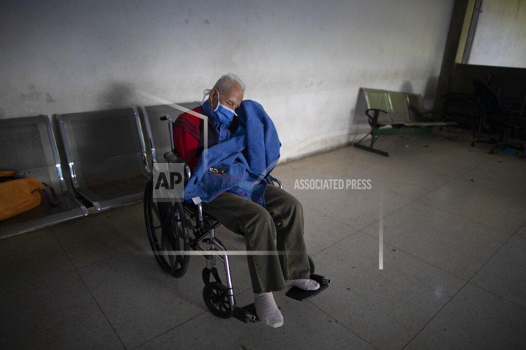 Ariana Cubillos Gavino Suazo waits in a wheelchair to be admitted to the COVID–19 wing at José Gregorio Hernández Hospital, a public hospital where doctors diagnosed him with a lung infection in the Catia neighborhood of Caracas, Venezuela, Monday, Sept. 21, 2020. The 76-year-old retired foreman at a clothing factory with six children and 19 grandchildren fell two years ago and hit his head, never regaining his speech and has been homebound despite surgeries. He was discharged after nearly two weeks at the hospital, where his daughter entered daily to feed and bathe him amid a shortage of health workers. (AP Photo/Ariana Cubillos)