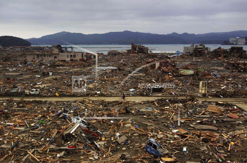 David Guttenfelder FILE - In this March 15, 2011, file photo, a Japanese survivor of an earthquake and tsunami rides his bicycle through the leveled city of Minamisanriku, Miyagi prefecture, northeastern Japan. March 11, 2021 marks the 10th anniversary of the massive earthquake, tsunami and nuclear disaster that struck Japan's northeastern coast. (AP Photo/David Guttenfelder, File)