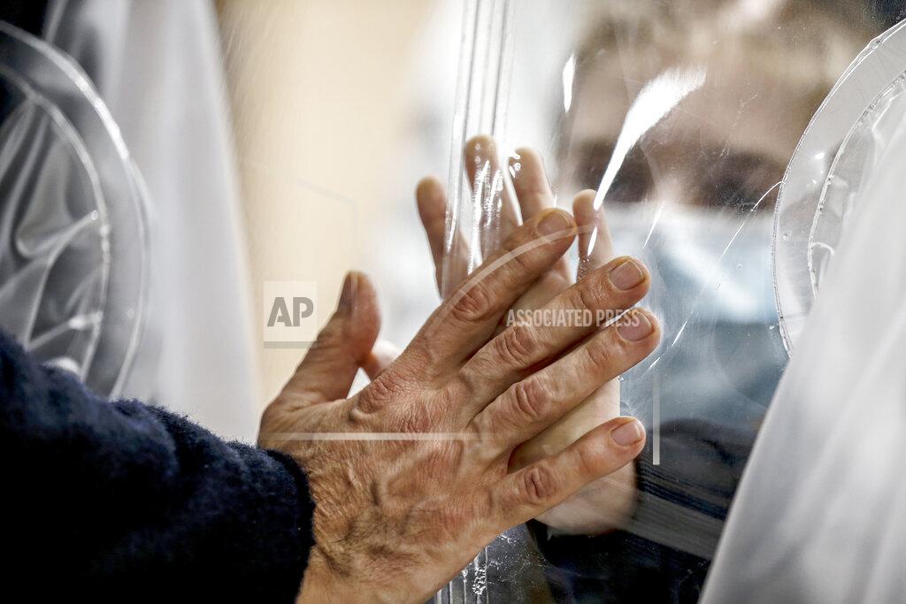 Cecilia Fabiano Relatives touch each other's hand through a plastic film screen and a glass to avoid contracting COVID-19 at the San Raffaele center in Rome, Tuesday, Dec. 22, 2020. Italians are easing into a holiday season full of restrictions, and already are barred from traveling to other regions except for valid reasons like work or health. Starting Christmas eve, travel beyond city or town borders also will be blocked, with some allowance for very limited personal visits in the same region. (Cecilia Fabiano/LaPresse via AP)