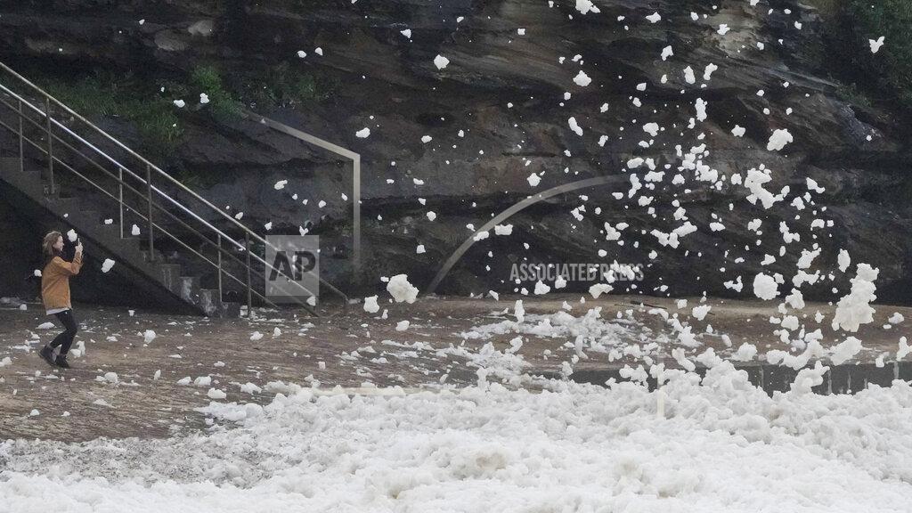 Mark Baker A woman films as sea foam is blown onto her at Bronte Beach as rain continues to fall in Sydney, Australia, Wednesday, July 6, 2022. More than 50,000 residents of Sydney and its surrounds have been told to evacuate or prepare to abandon their homes on Tuesday as Australia's largest city braces for what could be its worst flooding in 18 months. (AP Photo/Mark Baker)