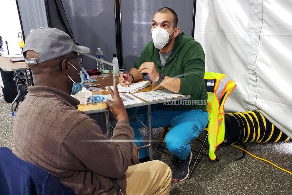 Uncredited In this March 12, 2021 photo provided by Unity Health Care, Othon Sosua, right, talks with a patient during a vaccination drive in Washington, D.C. Homeless Americans who have been left off priority lists for coronavirus vaccinations — or even bumped aside as states shifted eligibility to older age groups — are finally getting their shots as vaccine supplies increase. Walk-up vaccine events are crucial for a population with limited access to cars, cellphones or Wi-Fi, organizers say. (Unity Health Care via AP)