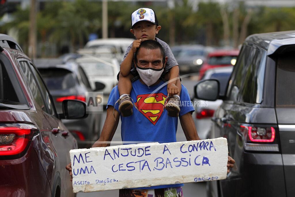 Eraldo Peres FILE - In this April 26, 2021 file photo, Jeferson Alves, 35, carries his 3-year-old son Jonathan Miguel on his shoulders when asking for a handout, as he holds a sign written in Portuguese that reads "Help me buy a basic food basket. Thank you," on an avenue in Brasilia, Brazil. Alves says he worked at a construction company for two years and that at the end of last year he was fired because of the pandemic. Now he seeks donations and money on the streets to support his family. (AP Photo/Eraldo Peres, File)