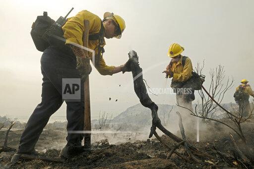 County of Santa Barbara Fire Department firefighters extinguish a roadside fire off the U.S. 101 highway Wednesday, Oct. 13, 2021, in Goleta, Calif. A wildfire raging through Southern California coastal mountains threatened ranches and rural homes and kept a major highway shut down Wednesday as the fire-scarred state faced a new round of dry winds that raise risk of flames. (AP Photo/Ringo H.W. Chiu)