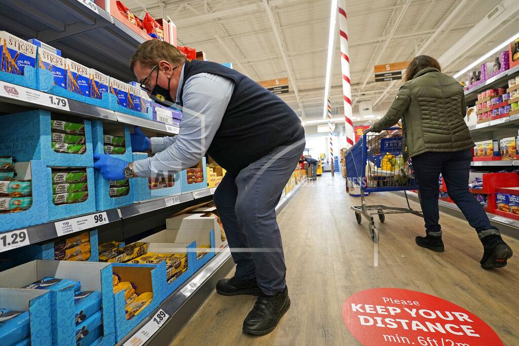 Kathy Willens In this Thursday, Feb. 4, 2021 photo, grocery supervisor Joseph Lupo, left, arranges cookies in the shelves at the Lidl food market in Lake Grove, N.Y., where he works after getting the first dose of the COVID-19 vaccination earlier in the day. Lupo, who fell ill with the virus in March, was elated to get his first vaccine dose. "I never ever want to get COVID again, or see anybody else get it," said Lupo, 59. (AP Photo/Kathy Willens)
