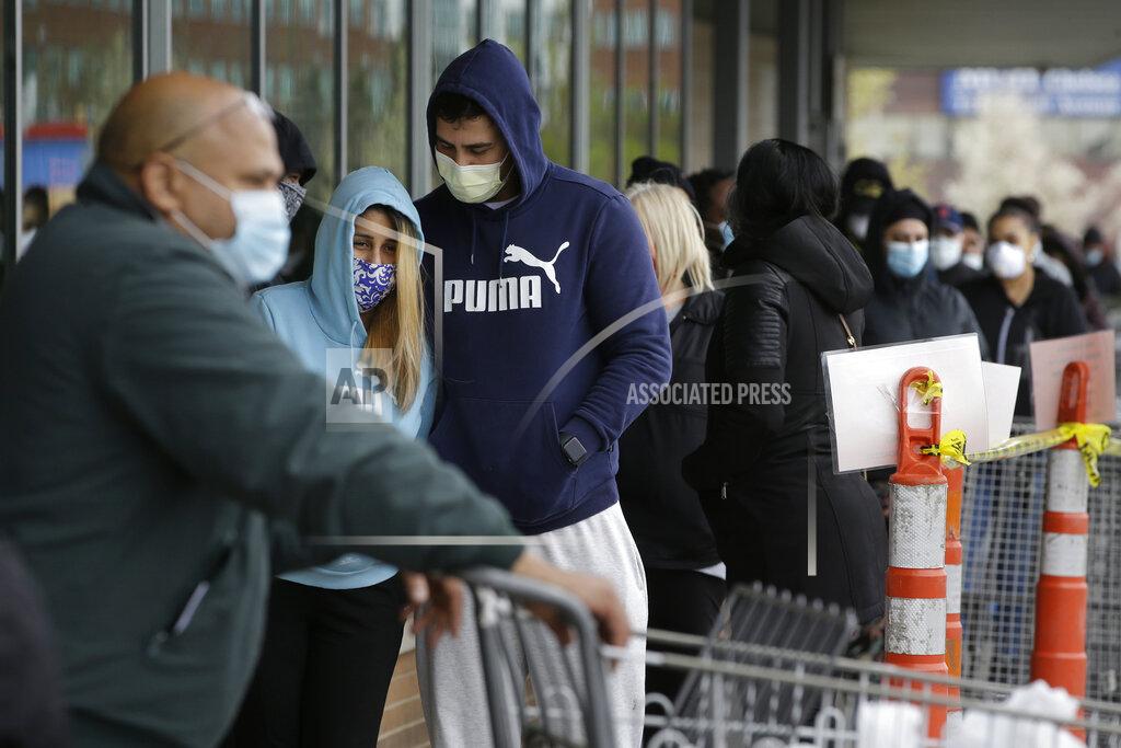 People wear face masks out of concern for the coronavirus as they wait to enter a supermarket Sunday, April 26, 2020, in Chelsea, Mass. (AP Photo/Steven Senne)