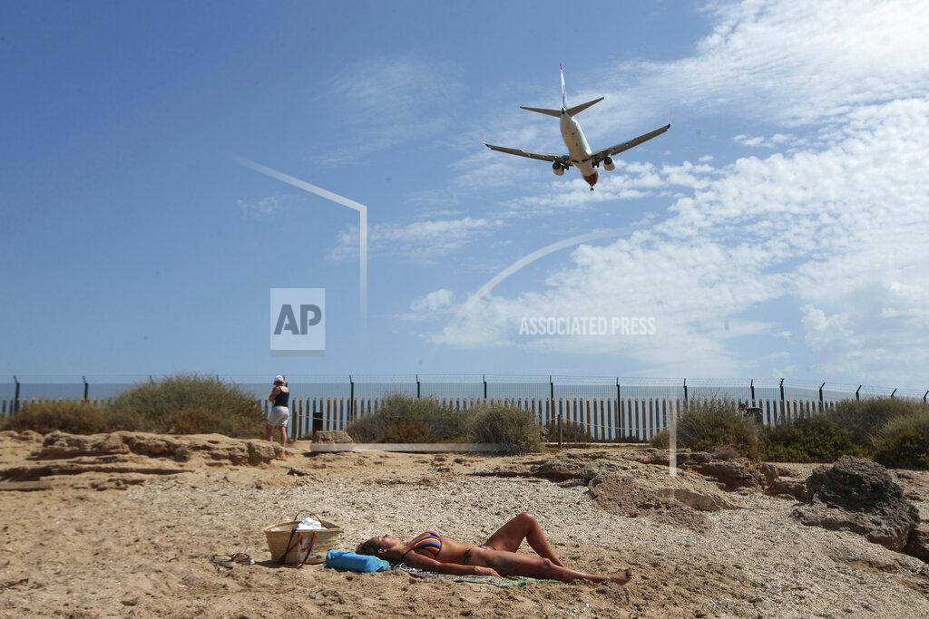 FILE - In this Wednesday, July 29, 2020 file photo, a woman sunbathes on the beach as an airplane lands at the Balearic Islands capital of Palma de Mallorca, Spain. Faced with a possible flood of visitors from Germany later this month, authorities in Spain’s Balearic Islands are warning hotel owners that tourists must adhere to coronavirus restrictions the same way residents do. The archipelago in the Mediterranean Sea is strengthening measures to combat the virus before the Easter period. But the restrictions haven’t stopped eager German tourists who have rushed to book flights and accommodation this week following their government’s removal of the islands from a list of high-risk contagion zones. (AP Photo/Joan Mateu, File)