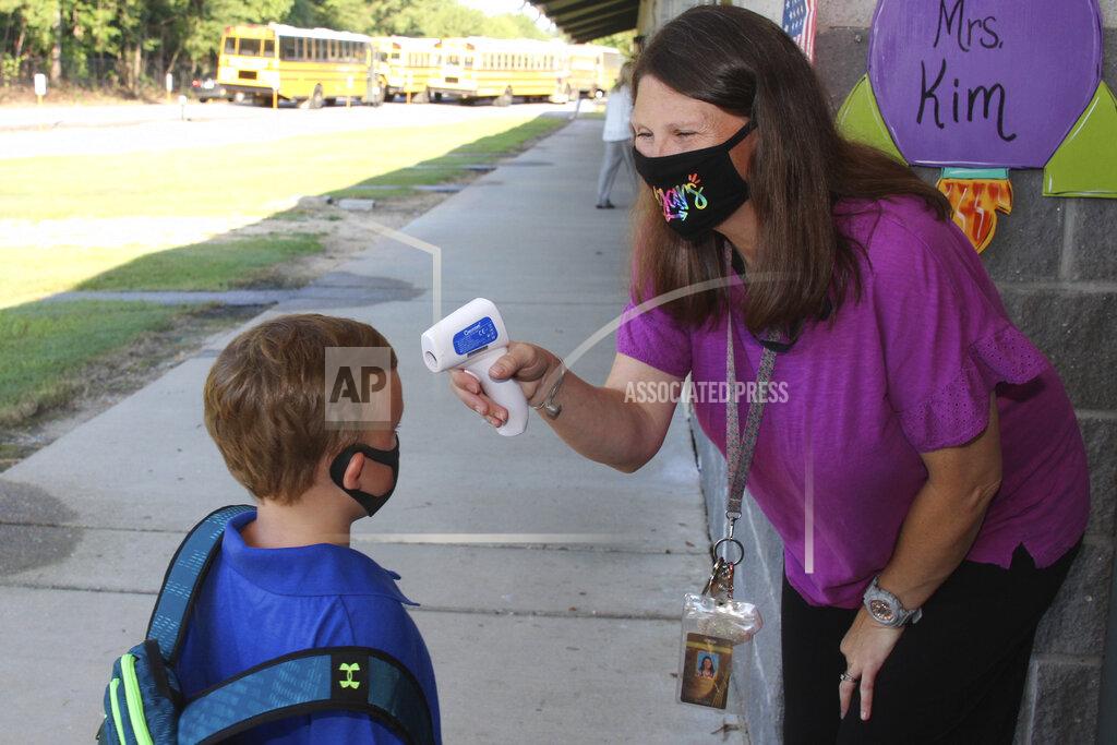 Janine Vincent In a photo provided by Newton County Schools, teaching assistant Crystal May talks to kindergarten student Lewis Henry Thompson, 5, as she takes his temperature at Newton County Elementary School in Decatur, Miss., Monday, Aug. 3, 2020. Thousands of students across the nation resumed in-person school Monday for the first time since March. Parents are having to balance the children's need for socialization and instruction that school provides, with the reality that the U.S. death toll from the coronavirus has hit about 155,000 and cases are rising in numerous places. (Janine Vincent/Newton County Schools via AP)