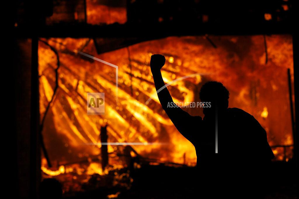 Julio Cortez A protester gestures in front of the burning 3rd Precinct building of the Minneapolis Police Department on Thursday, May 28, 2020, in Minneapolis. Protests over the death of George Floyd, a black man who died in police custody Monday, broke out in Minneapolis for a third straight night. (AP Photo/Julio Cortez)
