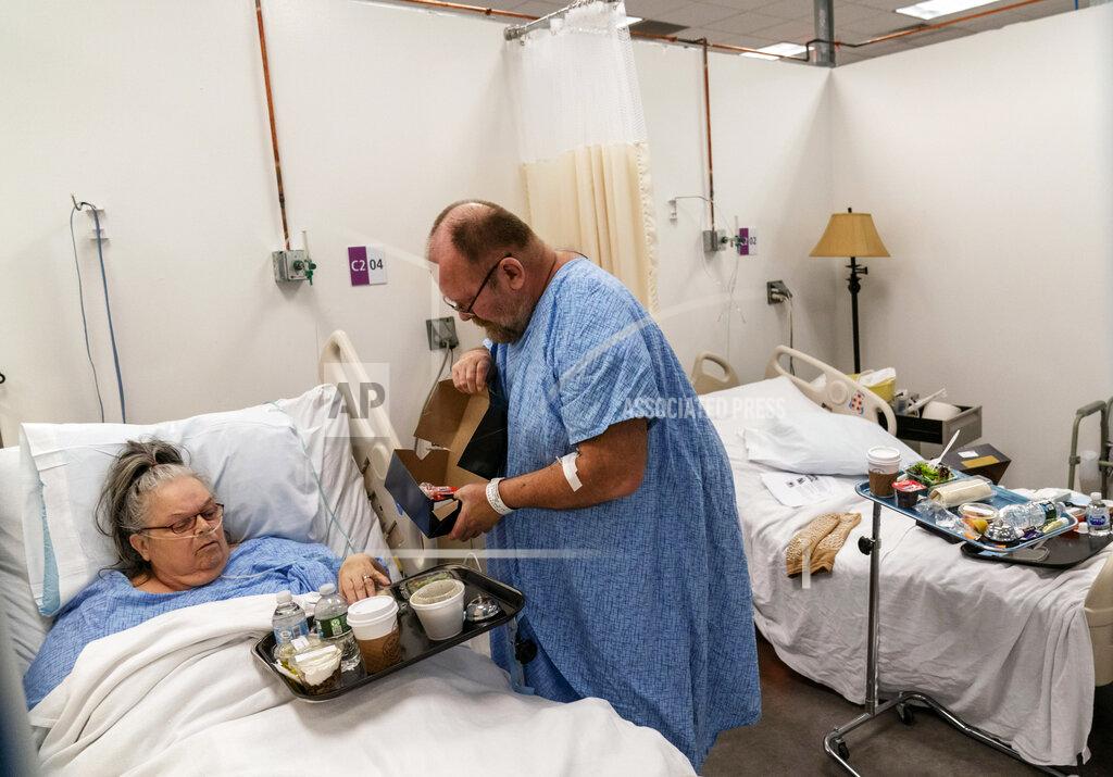 David Goldman Peter Sorrow, 62, right, helps his wife, Pauline, 71, with her lunch, as they both recover from COVID-19 at a field hospital operated by Care New England to handle a surge of COVID-19 patients, Wednesday, Feb. 10, 2021, in Cranston, R.I. "We're inspiration for each other," said Peter of being able to recover next to her in what staff calls "the honeymoon suite." "Just being here cheered her up." He now helps care for her: opening a stubborn lid on her lunch, cleaning a spot of food off her gown, updating their family. (AP Photo/David Goldman)