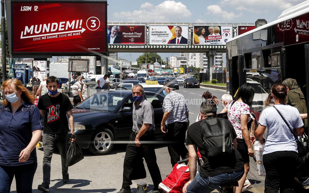 Boris Grdanoski People wearing face masks exit a bus as various electoral campaign posters are displayed in a street in Skopje, North Macedonia on Saturday, July 11, 2020. North Macedonia holds its first parliamentary election under its new country name this week, with voters heading to the polls during an alarming spike of coronavirus cases in the small Balkan nation. (AP Photo/Boris Grdanoski)
