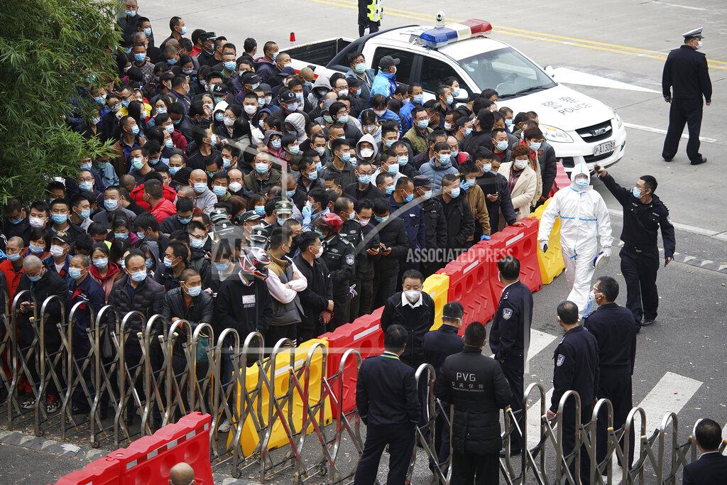 Uncredited Police and security officers wearing face masks to help curb the spread of the coronavirus stand guard as masked airport workers wait for COVID-19 testings at the Shanghai Pudong International Airport in Shanghai, Monday, Nov. 23, 2020. Chinese authorities are testing millions of people, imposing lockdowns and shutting down schools after multiple locally transmitted coronavirus cases were discovered in three cities across the country last week. (AP Photo)