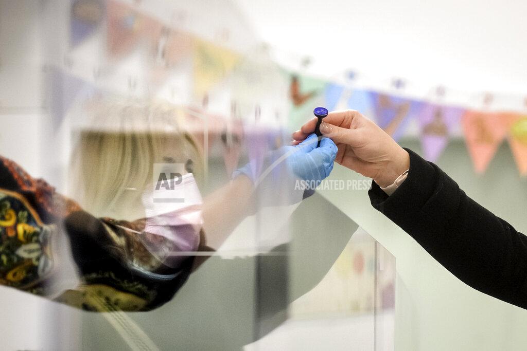 Alexandru Dobre An election official hands a voting stamp to a voter from behind a plastic screen in Bucharest, Romania, Sunday, Dec. 6, 2020. Voting started in Romania's legislative election expected to restore some measure of stability after five years of political and social turbulence with more than 18 million Romanians registered to vote for a new legislative body. (AP Photo/Alexandru Dobre)