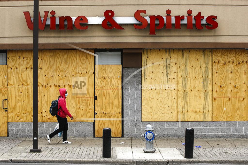 A person wearing a protective face mask as a precaution against the coronavirus walks past a boarded up Wine and Spirits store in Philadelphia, Thursday, April 16, 2020. Pennsylvania's liquor agency says workers are coming back on the job at more than 100 shuttered state-owned liquor stores to help process online orders. (AP Photo/Matt Rourke)