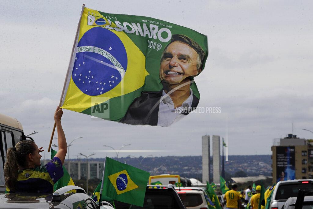 Eraldo Peres A demonstrator waves a banner with an image of President Jair Bolsonaro, during a caravan backing Bolsonaro’s anti-coronavirus-lockdown stance, marking May Day, or International Workers' Day, in Brasilia, Brazil, Saturday, May 1, 2021. (AP Photo/Eraldo Peres)