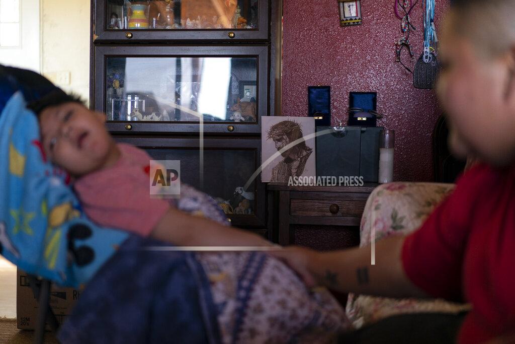 Carolyn Kaster On a small table next to an image of Jesus in a crown of thorns, the ashes of Gloria Uriarte, right and her mother, Eva Dinehdeal, are displayed on a table in Tuba City, Ariz., on April 22, 2020. In the foreground at left is Gloria's son, Curly, as his aunt Christina Dinehdeal holds his hand. The Navajo reservation has some of the highest rates of coronavirus in the country. If Navajos are susceptible to the virus' spread in part because they are so closely knit, that's also how many believe they will beat it. (AP Photo/Carolyn Kaster)