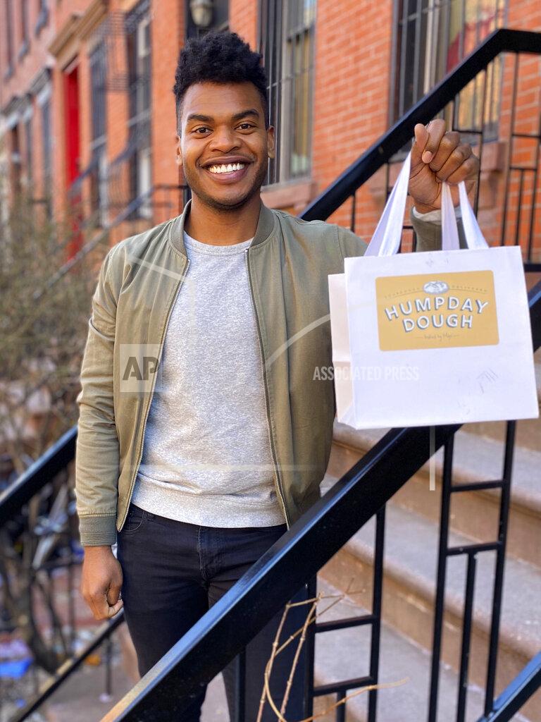 Michael Lowney Broadway performer Max Kumangai holds a bag promoting his company Humpday Dough in New York. The triple threat from the musical “Jagged Little Pill” has leaned into a fourth skill as the pandemic marches on: baking and selling his own sourdough. (Michael Lowney/Humpday Dough via AP)